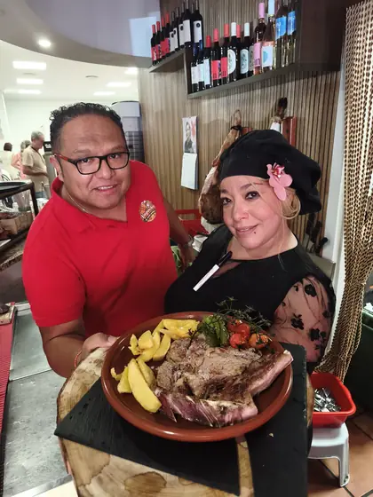 El dueño y una cocinera con una cazuela de carne asada, patatas y verduras