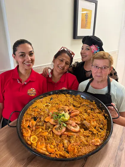 Cuatro trabajadoras del bar sonriendo detrás de una paella con gambas
